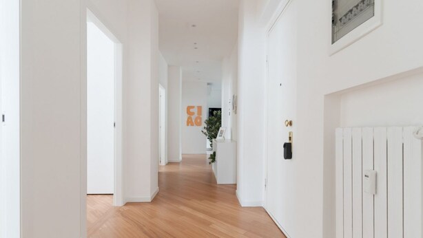 A hallway with white walls, wooden flooring, and a radiator on the right. - GuestHost - A modern and spacious 142 square meters apartment, perfect for five people, located on the second floor of a building with an elevator (NOT accessible to guests with disabilities).The property is just steps from the S. Agostino metro station, (Milan)