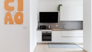 A modern kitchen with white cabinets, a flat-screen TV, a coffee maker, and a small oven. - GuestHost - A modern and spacious 142 square meters apartment, perfect for five people, located on the second floor of a building with an elevator (NOT accessible to guests with disabilities).The property is just steps from the S. Agostino metro station, (Milan)