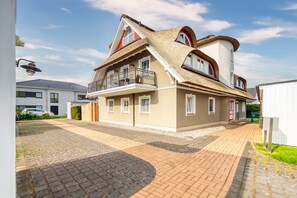 Ein zweistöckiges Haus mit Balkon, Auffahrt und einem angrenzenden Gebäude.
