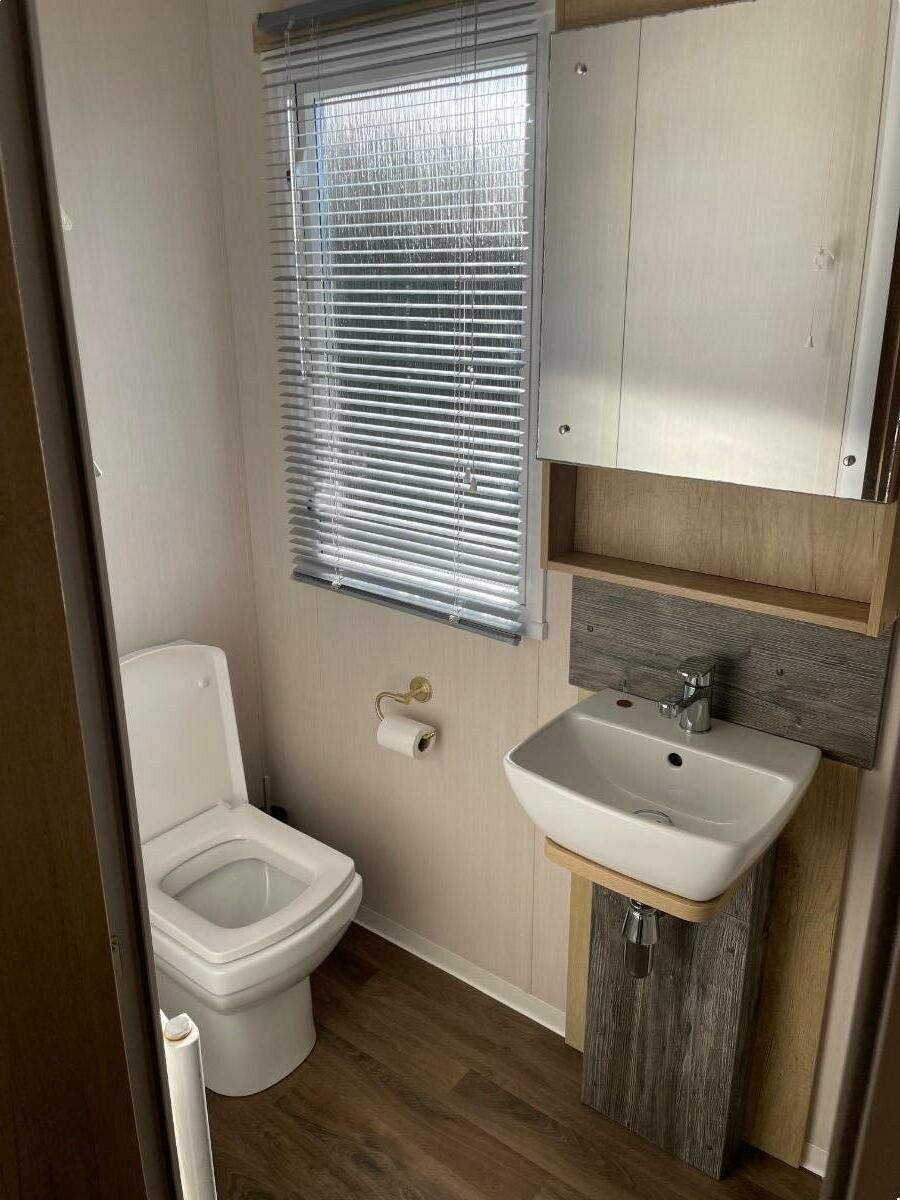 A compact bathroom with a toilet, a sink, and a window with blinds.