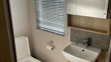 A compact bathroom with a toilet, a sink, and a window with blinds.