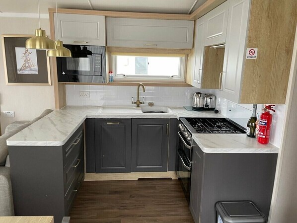 A compact kitchen with a sink, stove, and cabinets, featuring a window above the sink and a pendant light.