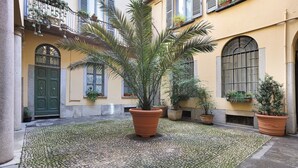 Une cour intérieure agrémentée d’un palmier, de plantes en pot et d’un sol pavé.