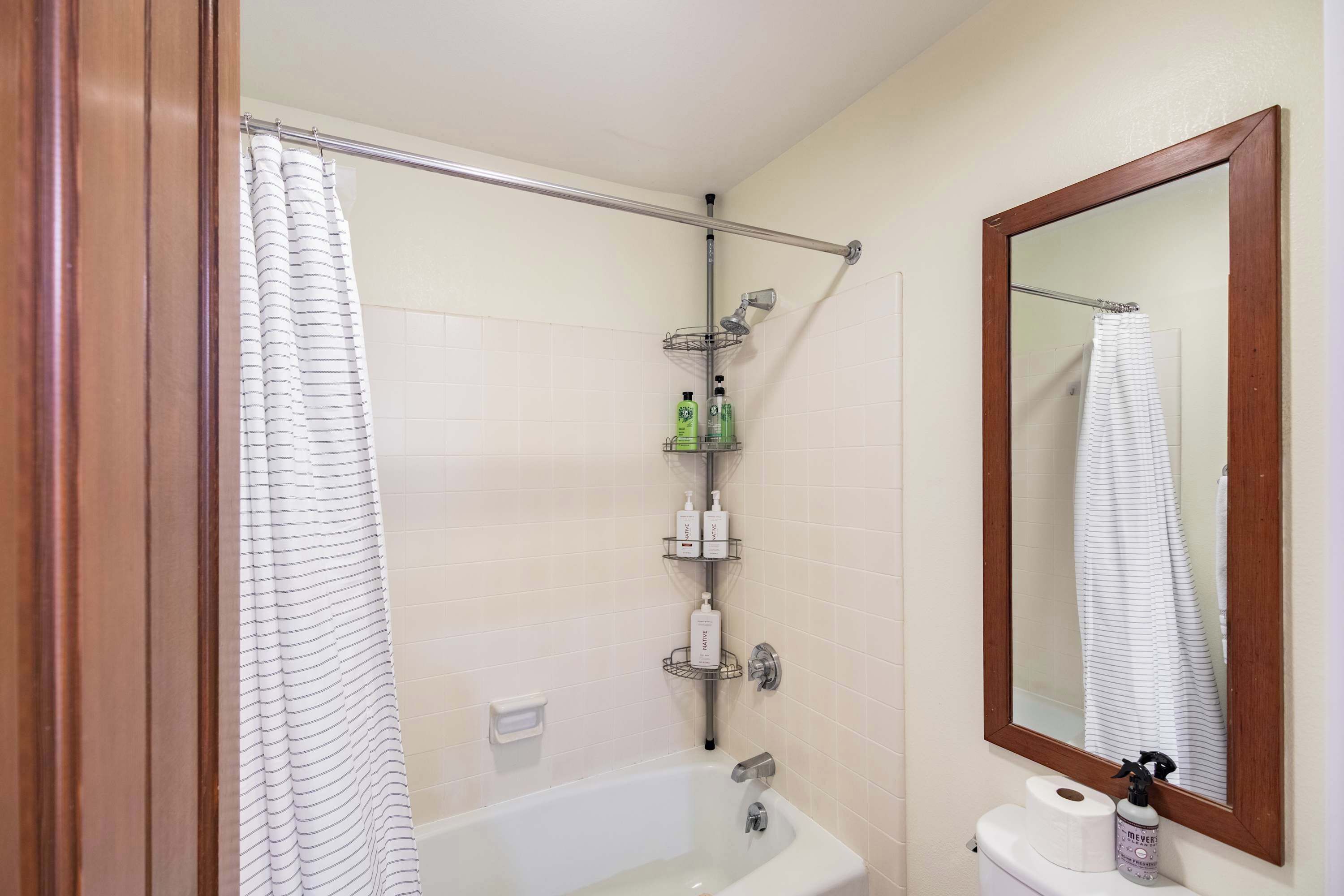 A bathroom with a bathtub, a shower curtain, a towel rack, and a mirror.