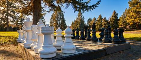 A large outdoor chess set on a paved area surrounded by trees.