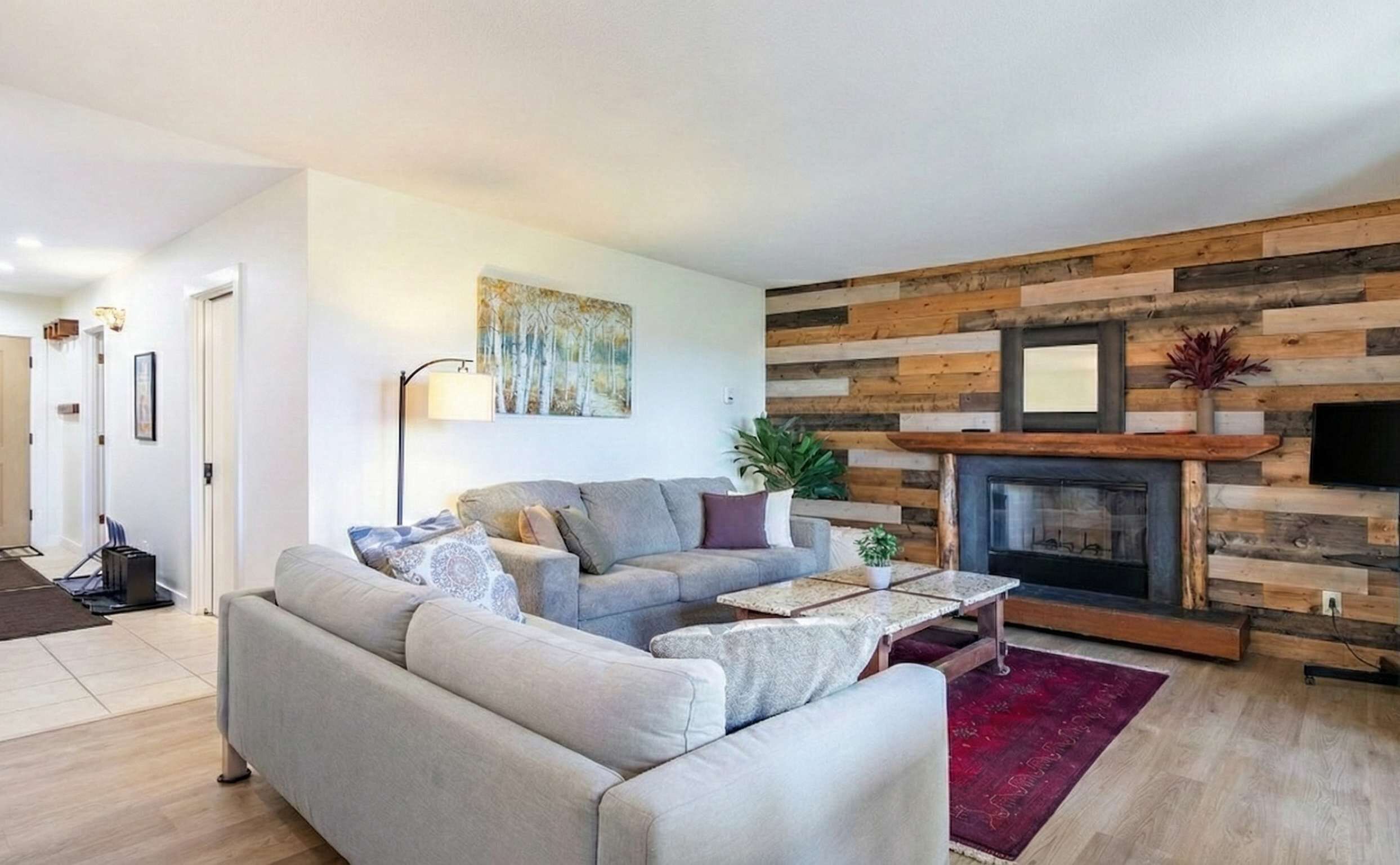 Una sala de estar con un sofá gris, una mesa de centro, una chimenea y una pared de madera.