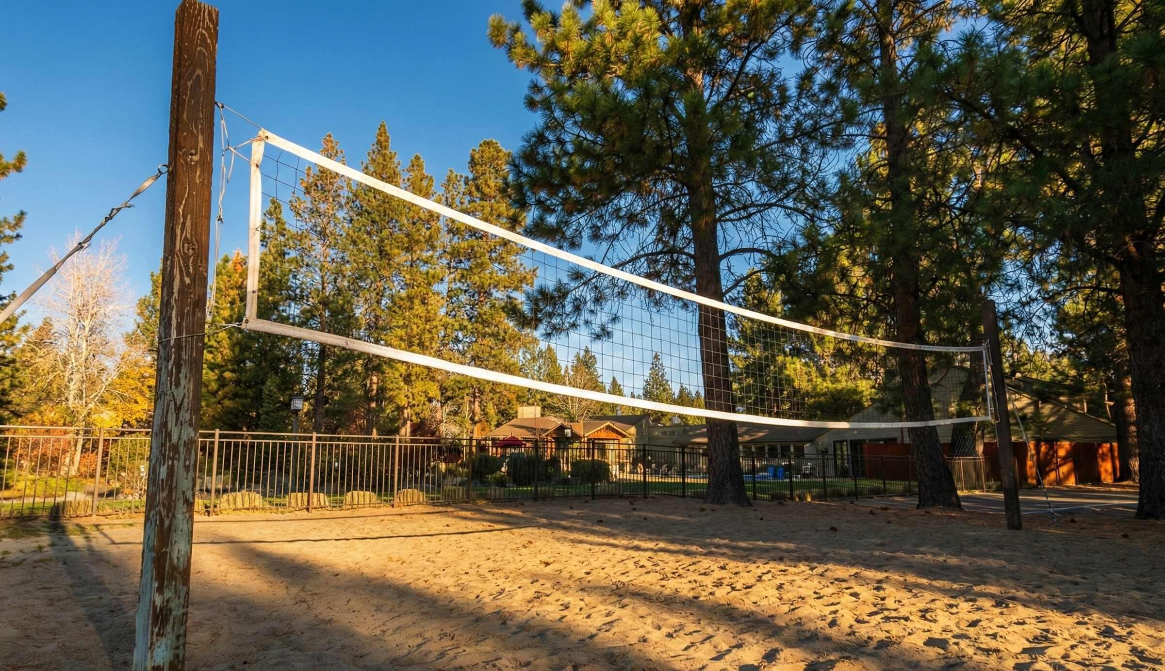 Un terrain de volleyball de sable avec un filet, entouré d’arbres et d’une clôture.