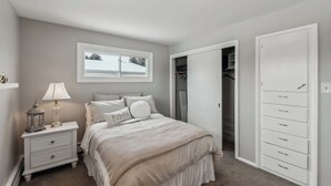 Une chambre à coucher comprenant un lit, une table de chevet, une lampe, une armoire et une fenêtre.