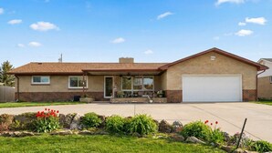 Une maison de plain-pied avec une façade en briques, un porche à l’avant doté de mobilier d’extérieur et un garage.