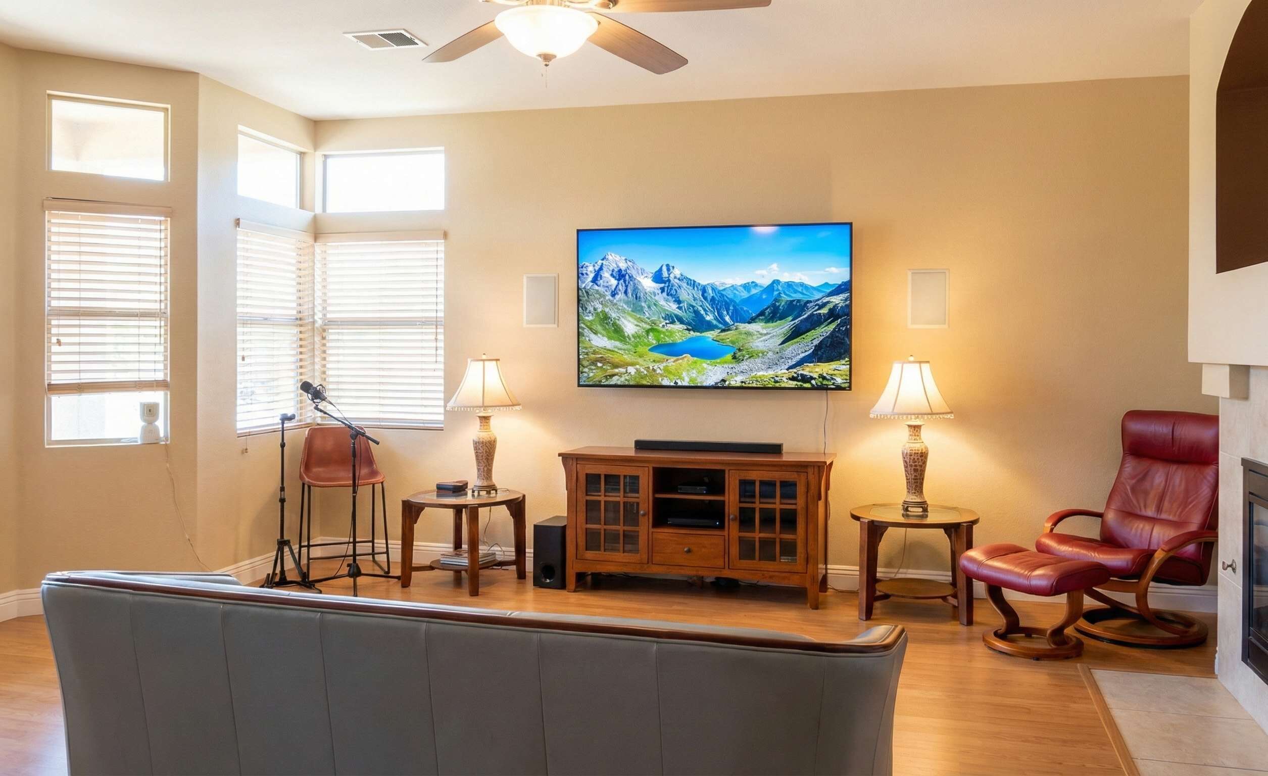Een woonkamer met een grote flatscreen televisie, twee lampen, een leren fauteuil en een houten kast.