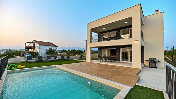 Ein modernes, zweistöckiges Haus mit Swimmingpool, Außenbereich zum Sitzen und Blick auf die Berge.
