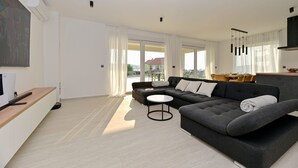 Ein modernes Wohnzimmer mit einer grauen Couch, einem kleinen runden Tisch und einem großen Fenster mit Vorhängen.