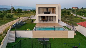 Ein modernes, zweistöckiges Haus mit Swimmingpool, Außenbereich zum Sitzen und Blick auf die umliegende Landschaft.