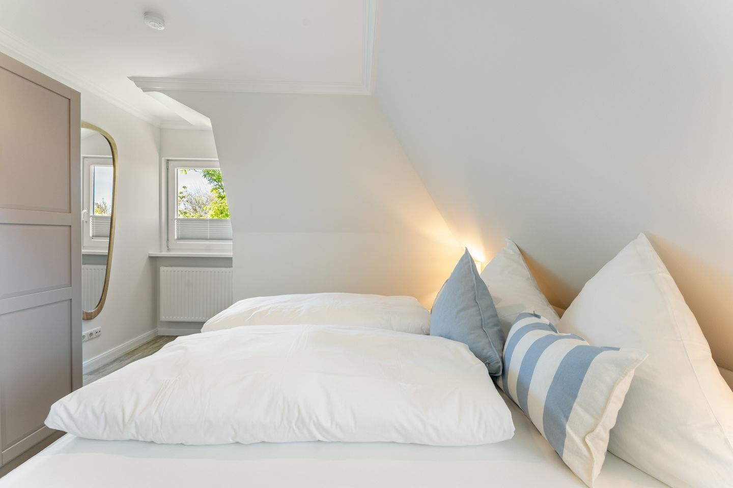 Een slaapkamer met een bed, kussens, een spiegel en een raam.