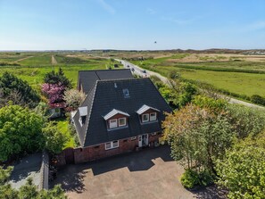 A two-story house with a paved driveway, surrounded by greenery and a clear sky. - House Jacobsen Strandgut - Newly renovated! Vacation apartment Haus Jacobsen Strandgut (Sylt)