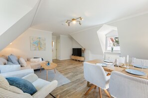 A modern loft apartment with a dining area, living room, and a TV in the background. - House Jacobsen Strandgut - Newly renovated! Vacation apartment Haus Jacobsen Strandgut (Sylt)