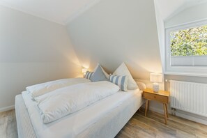 A bedroom with a bed, bedside lamps, a nightstand, and a window with a view of greenery. - House Jacobsen Strandgut - Newly renovated! Vacation apartment Haus Jacobsen Strandgut (Sylt)