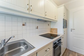 A kitchen with white cabinets, a stainless steel sink, a black induction cooktop, and a microwave. - House Jacobsen Strandgut - Newly renovated! Vacation apartment Haus Jacobsen Strandgut (Sylt)