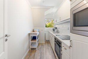A narrow kitchen with white cabinetry, a built-in oven, and a microwave. - Jacobsen Strandgut House - Recently Renovated! Haus Jacobsen Strandgut Vacation Apartment (Sylt)