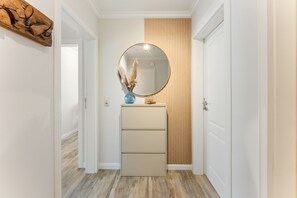 A hallway with a wooden floor, a beige dresser with drawers, a round mirror, and a vase with dried pampas grass. - Jacobsen Strandgut House - Recently Renovated! Haus Jacobsen Strandgut Vacation Apartment (Sylt)