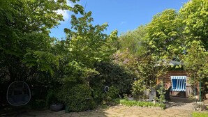 Jardí amb un camí de pedra, una cadira penjant i una zona d'estar coberta.