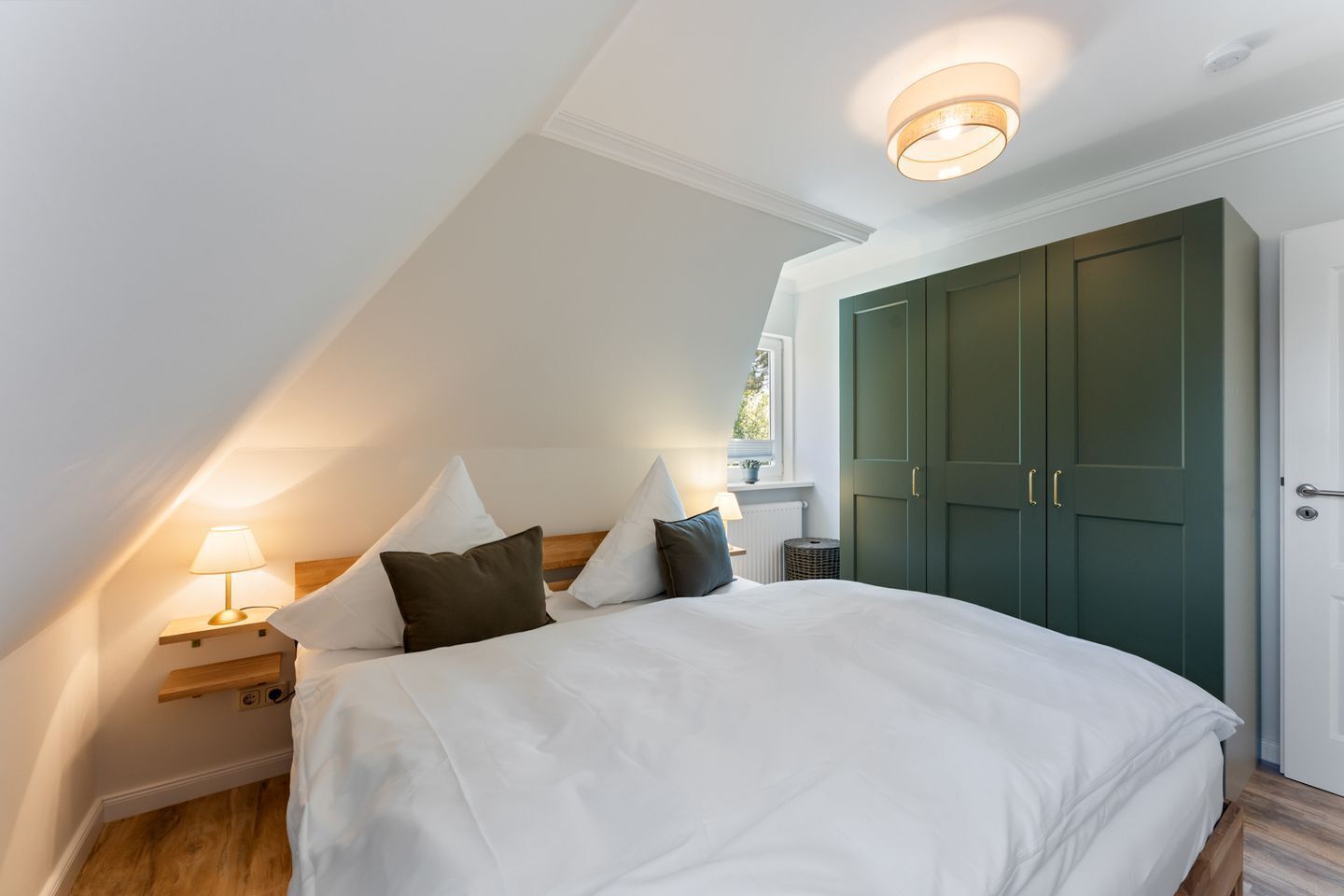 Une chambre à coucher avec un lit, des lampes de chevet, une fenêtre et une armoire verte.