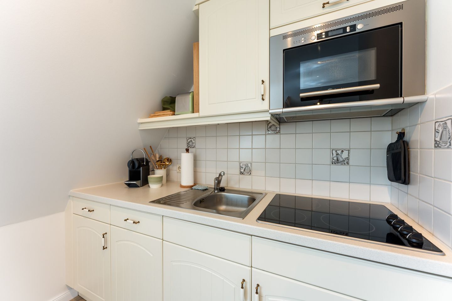 Ett kök med vita skåp, en diskho i rostfritt stål, en svart mikrovågsugn och en gasspis.