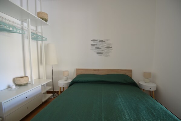 A bedroom with a bed, two bedside tables, a dresser, a lamp, and a wall art piece.