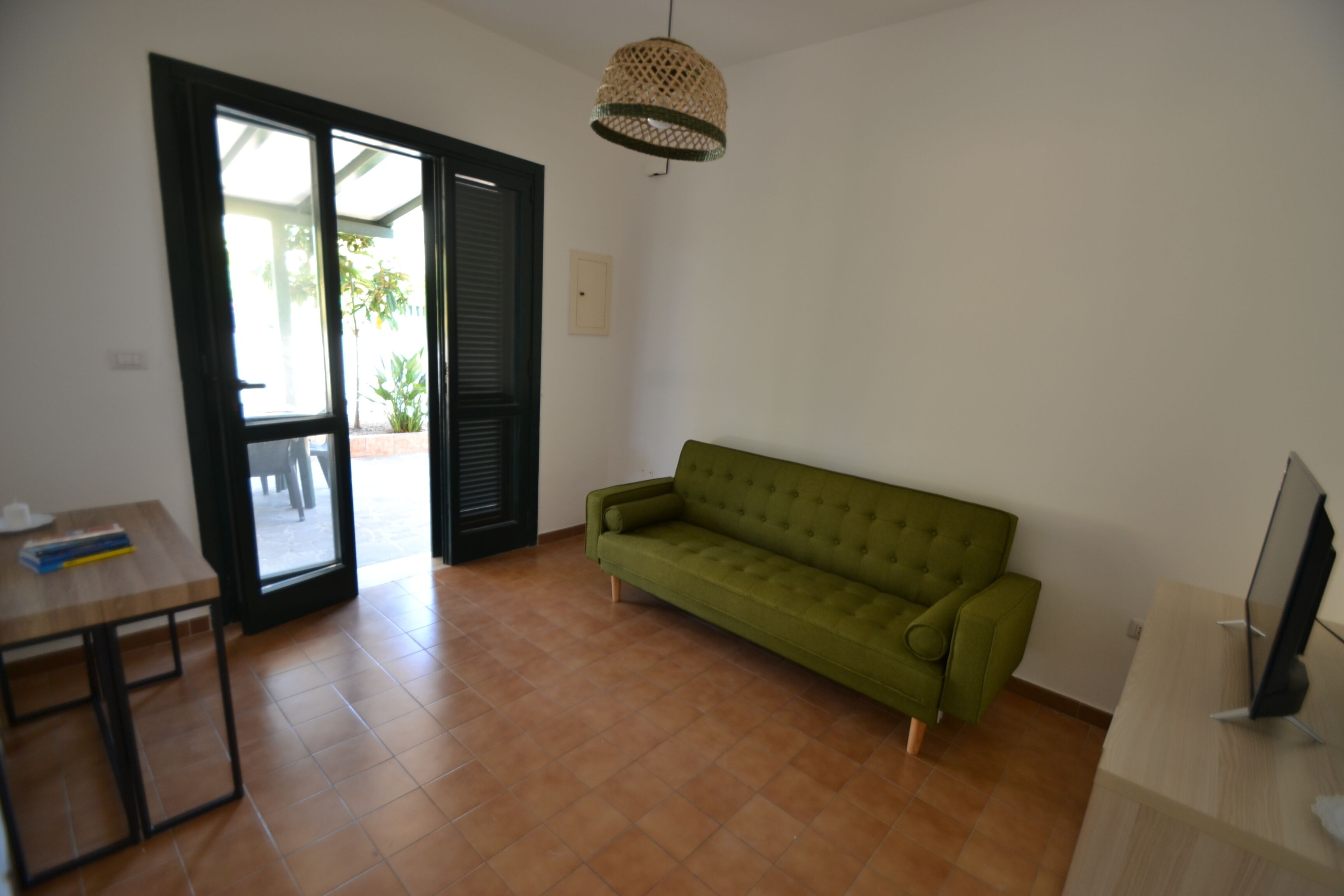 A room with a green sofa, a wooden table, a TV, and a door leading outside.