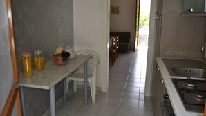 Ett kompakt kök med en bänkskiva i granit, en vit stol och ett matbord. Det finns en spis med ett handfat och ett skåp ovanför.