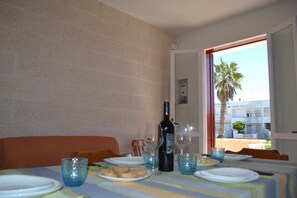 A dining table with plates, glasses, and a bottle of wine, set against a brick wall with a view of palm trees and buildings outside. - Casa Zoe in San Foca (San Foca)