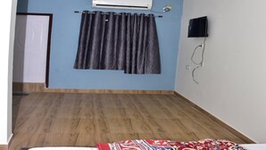 A bedroom with a bed, a ceiling fan, an air conditioning unit, a television mounted on the wall, and a patterned rug.