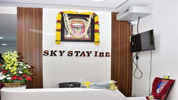 A reception desk at SKY STAY INN with a framed religious icon above it, a flat-screen TV mounted on the wall, and a bouquet of flowers on the counter.