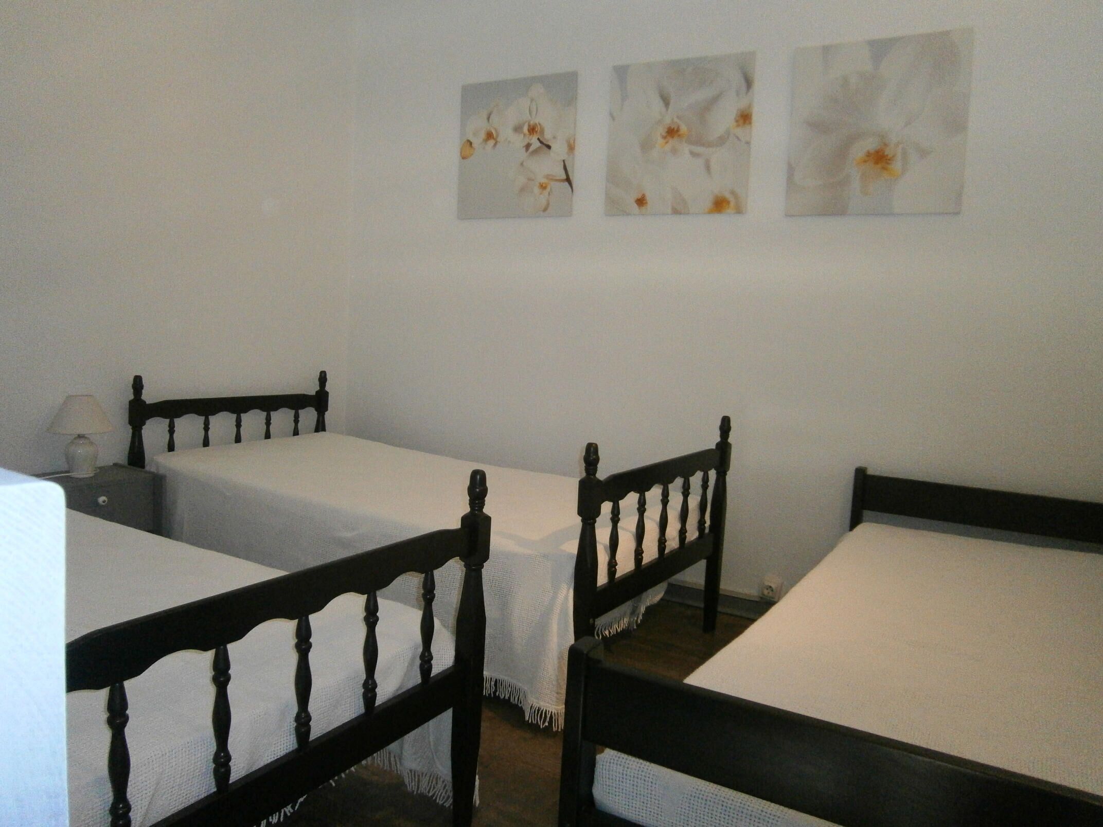 Une chambre avec deux lits simples, une table de chevet avec une lampe et trois tableaux encadrés au mur.