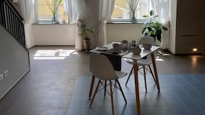Un coin repas avec une table dressée pour deux personnes, deux plantes en pot et un escalier sur le côté gauche.