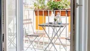Un balcon avec une table et des chaises, des plantes en pot et une vue sur la rue.