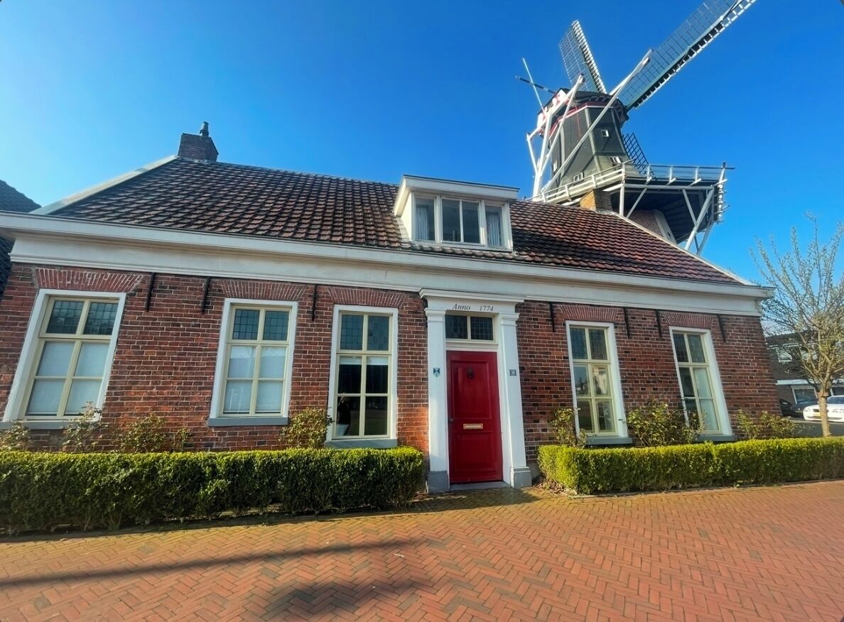 A brick building with a red door, windows, and a windmill in the background.