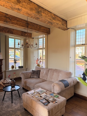 A cozy living room with a large sectional sofa, a small round table, and a chandelier. - Characterful miller's house next to the mill on the edge of downtown (Winschoten)