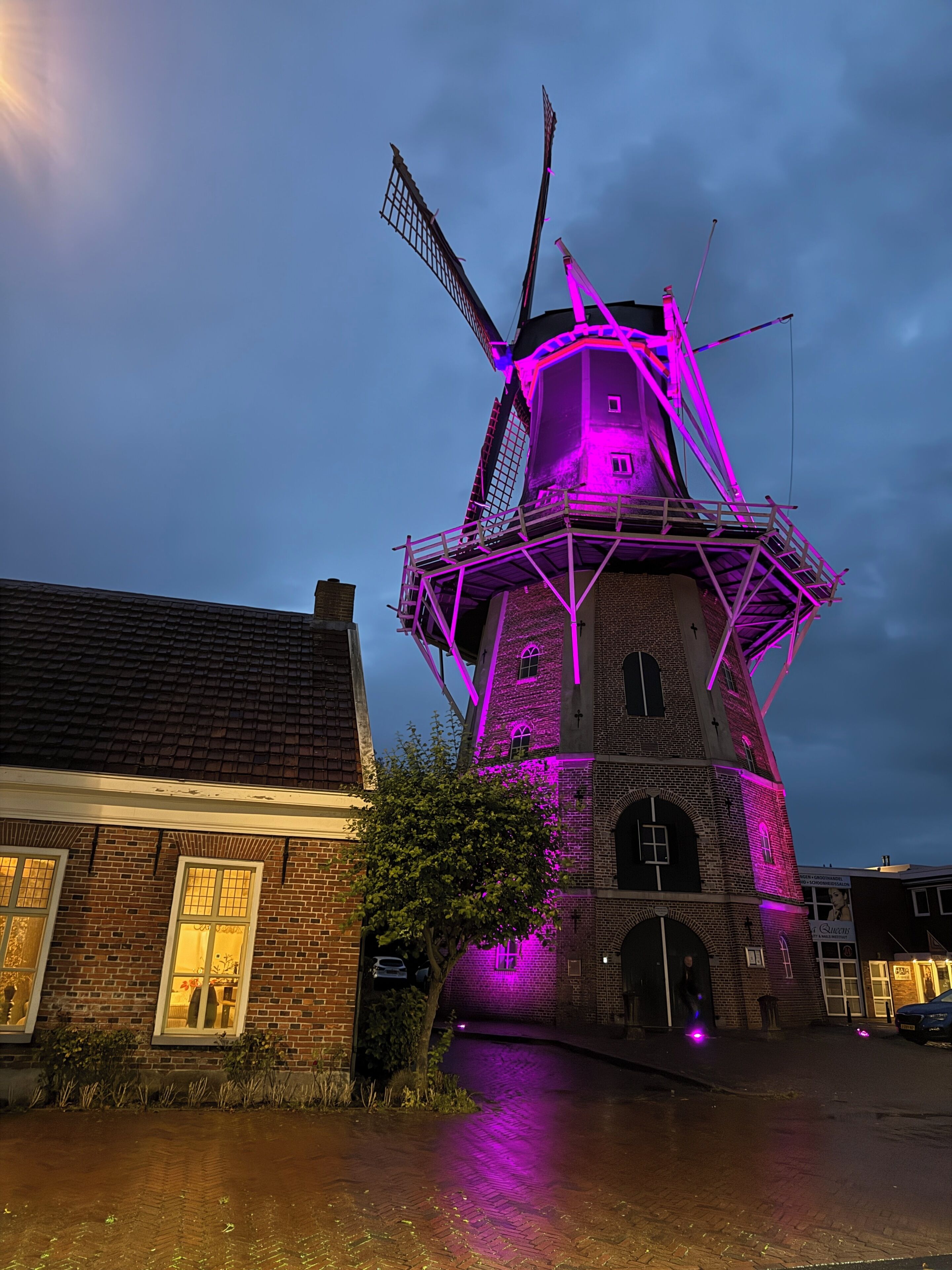 Een windmolen met een bakstenen fundering en een metalen top, verlicht met paarse lichten.