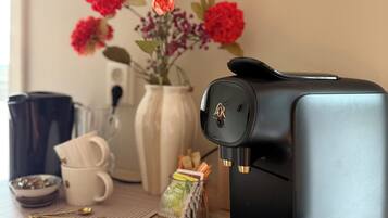 A coffee maker on a wooden table with a vase of flowers, a coffee cup, and a small bowl.