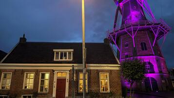 Un bâtiment en briques avec une porte et des fenêtres rouges, un lampadaire et un moulin à vent illuminé de lumière violette.