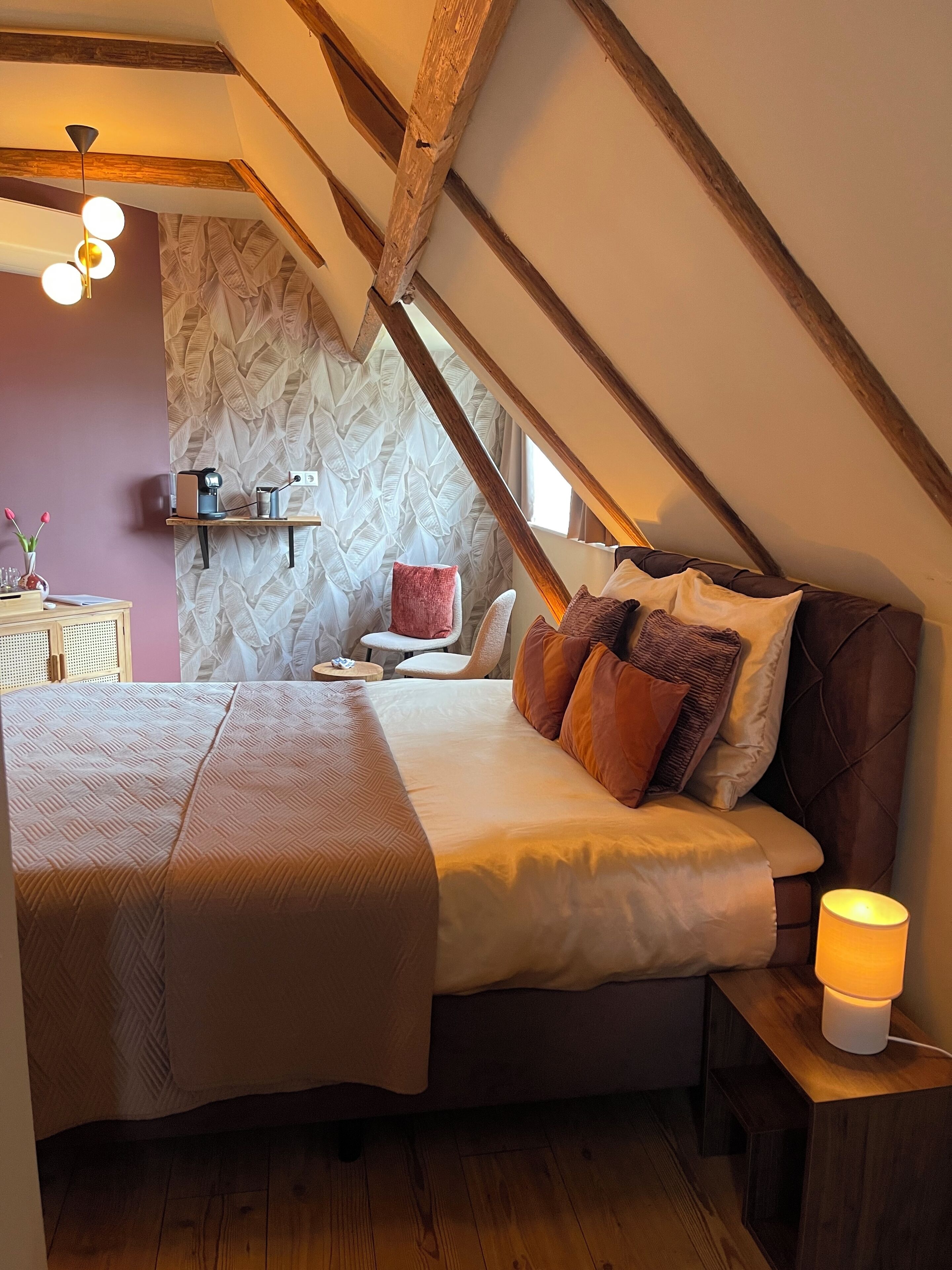 Ein Schlafzimmer mit einem großen Bett, Holzbalken, einer Wand mit Muster und einem Nachttisch mit Lampe.