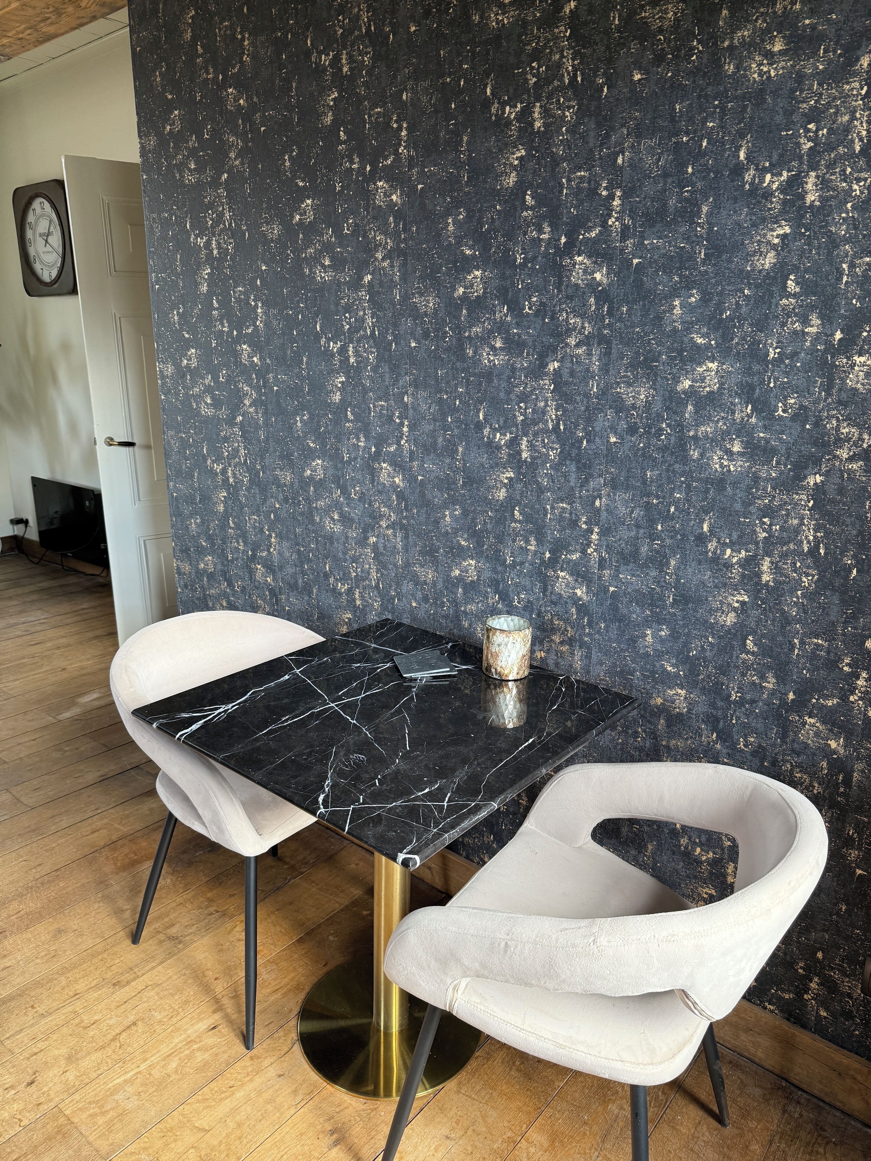 A modern dining area with a black marble table, two white upholstered chairs, and a textured dark wall.