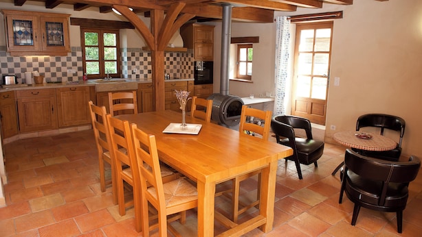 A spacious kitchen with wooden cabinets, a large dining table, and a built-in wood stove. - Gîte Petite Maison in the Gers countryside (Castelnau-sur-l'Auvignon)