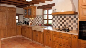 A kitchen with wooden cabinets, a tiled backsplash, and a black stove. - Gîte Petite Maison in the Gers countryside (Castelnau-sur-l'Auvignon)