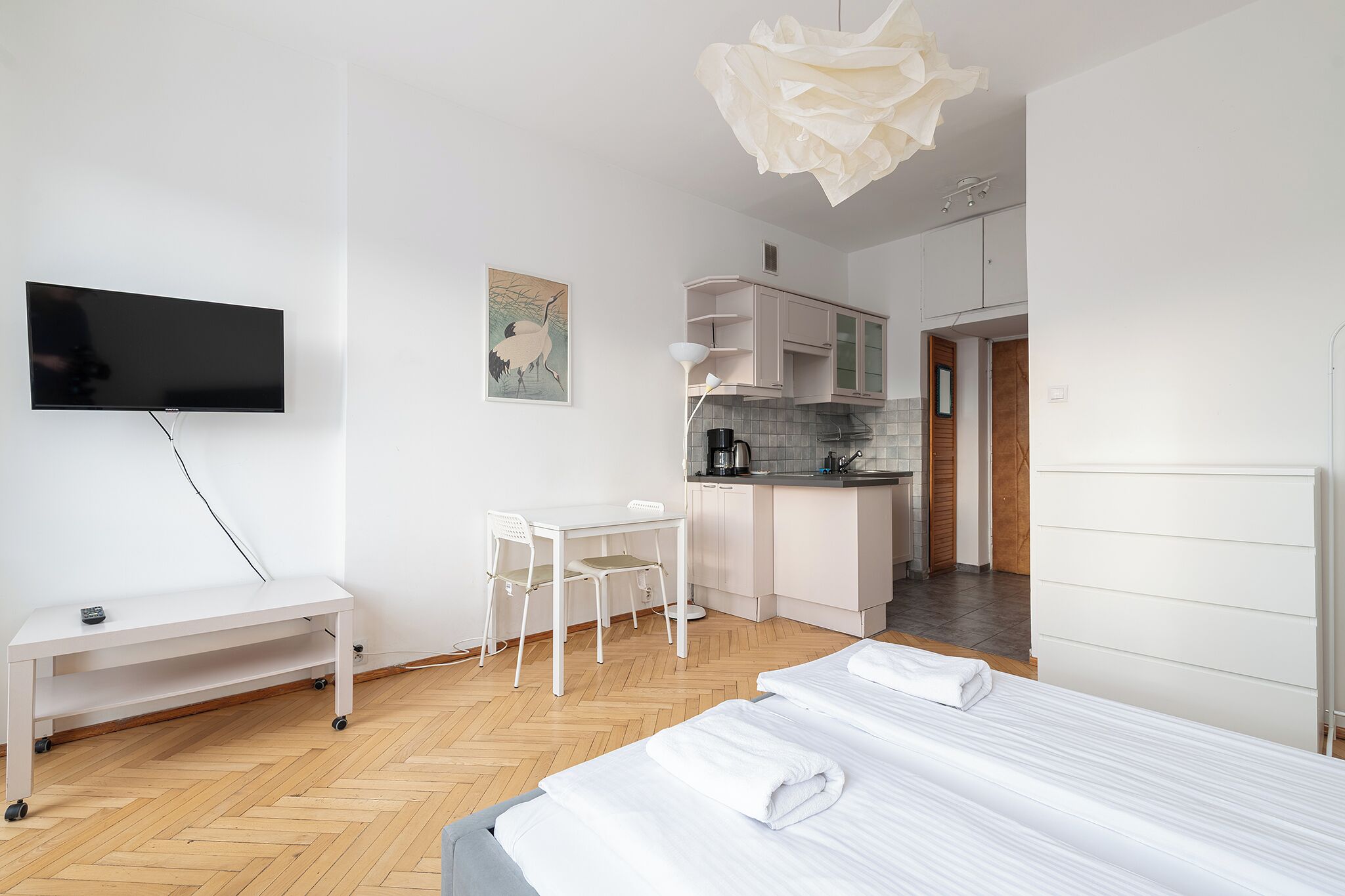 Una habitación de hotel moderna con televisión de pantalla plana, escritorio con sillas, kitchenette y cama con toallas.