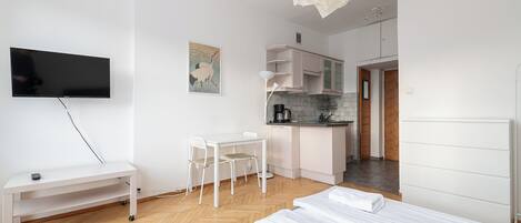 Una habitación de hotel moderna con televisión de pantalla plana, escritorio con sillas, kitchenette y cama con toallas.