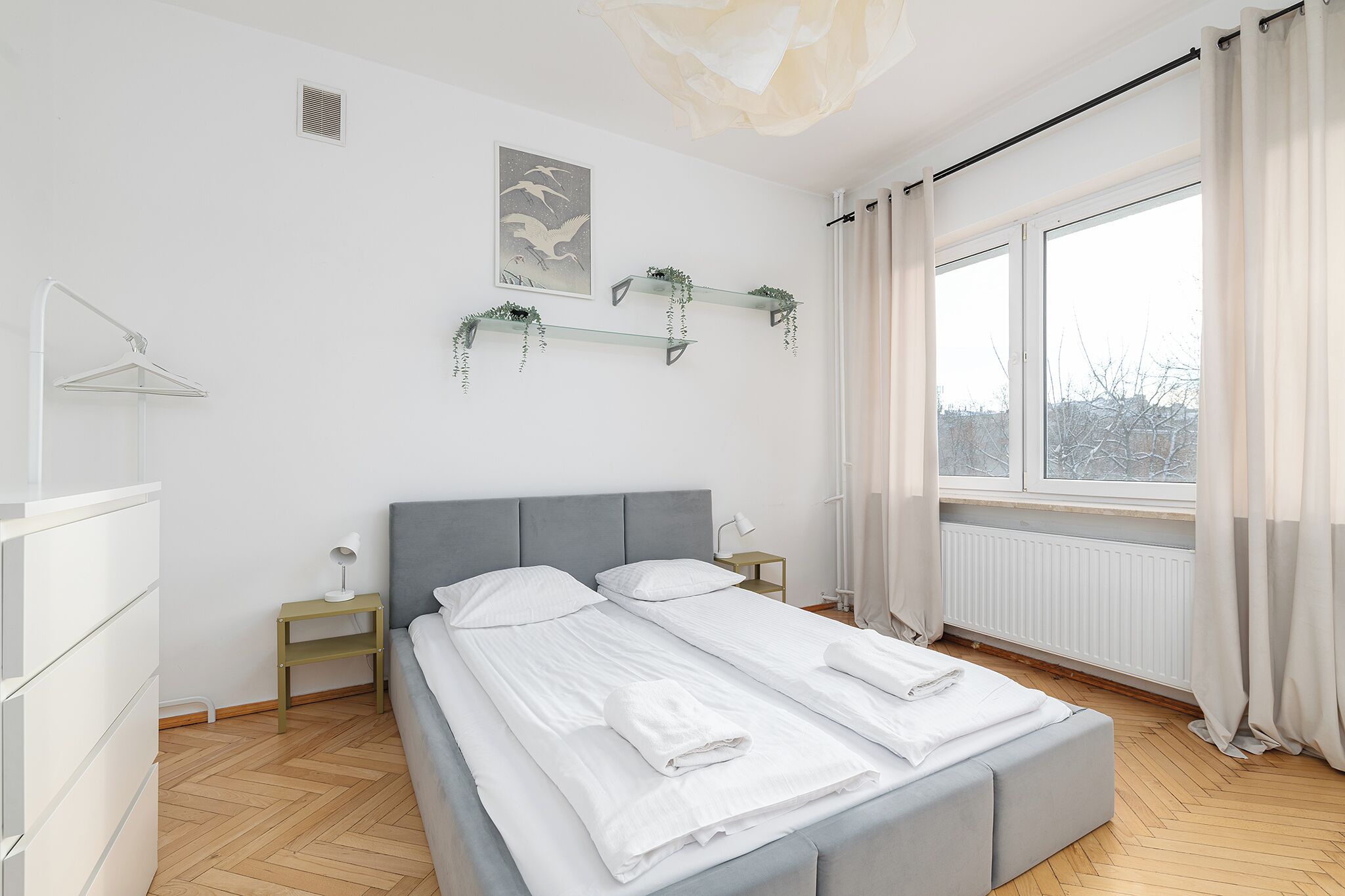 Ein modernes Schlafzimmer mit Bett, Nachttischen, einer Hängelampe und einem Fenster mit Vorhängen.