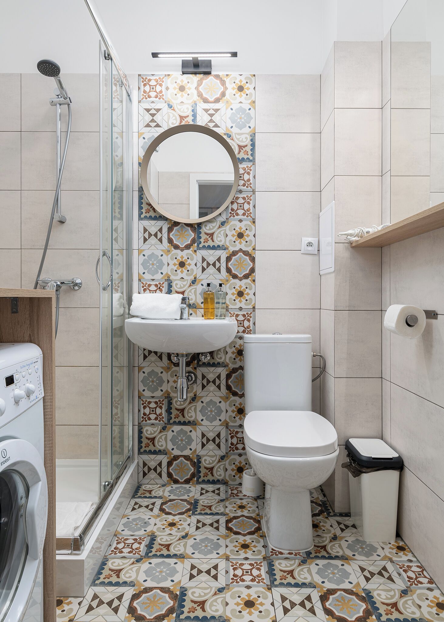 A bathroom with a shower, toilet, and sink, featuring patterned tiles and a mirror.
