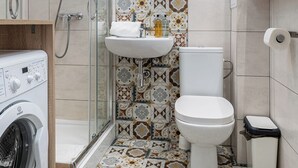 Un baño pequeño con ducha, inodoro, lavabo y lavadora.